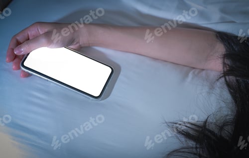 Preview: Working woman sleeping in bed at home and hand holding blank screen mobile phone. Woman using phone
