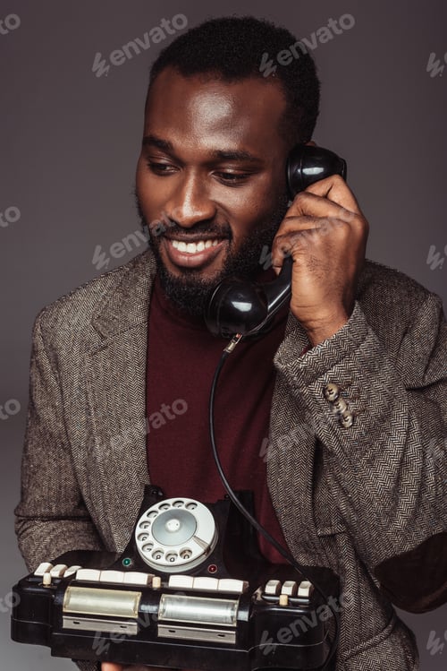 Preview: smiling african american retro styled man talking by vintage stationary telephone isolated on grey