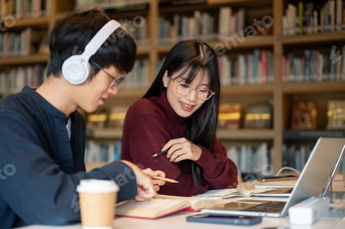 Preview: Glasses asian woman student looking at man friend's notebook aside laptop while sit at library table