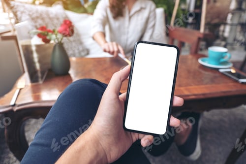 Preview: a man holding black mobile phone with blank white screen with woman sitting in cafe