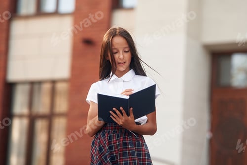 Visualização: Concepção de conhecimento. Menina da escola em uniforme está ao ar livre perto do prédio