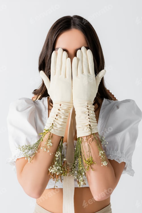 Preview: young woman covering face with hands in gloves and flowers isolated on white