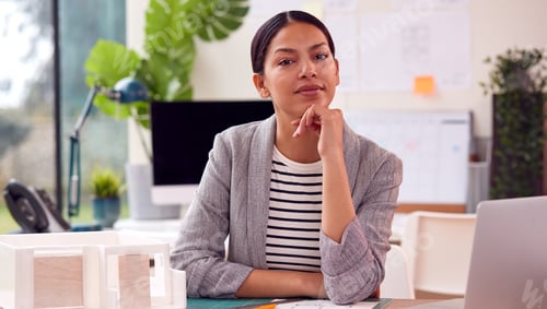 Preview: Portrait Of Female Architect In Office Sitting At Desk With Model Of New Building