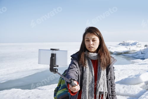 Preview: Female traveler outdoors at icy landscape using monopod to make selfie picture