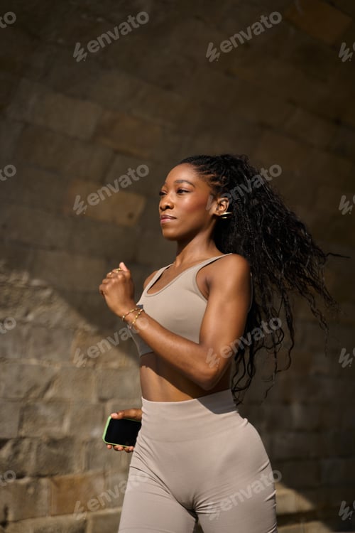 Preview: Young sporty woman running outdoors holding smartphone