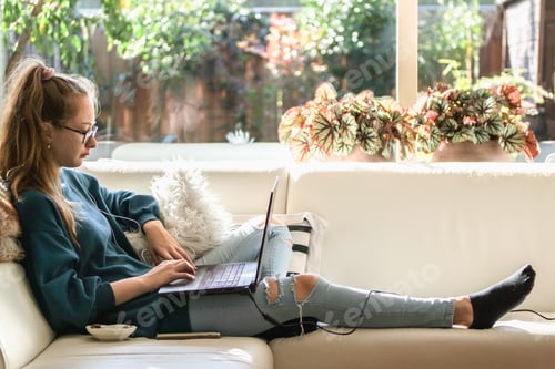 Preview: Generation x girl using laptop. Sitting on the couch in the living room with big windows.