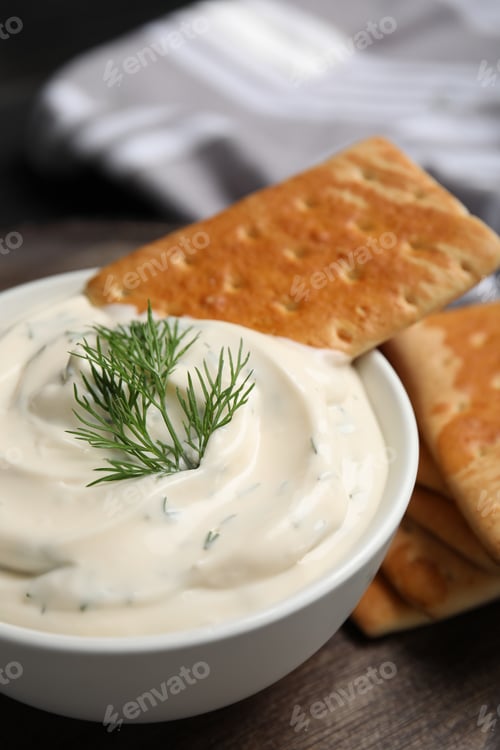 Preview: Tasty creamy dill sauce with cracker in bowl on black wooden table, closeup