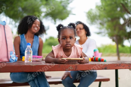 Preview: Little girl using tablet at park with family watching