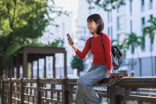 Preview: Young asian woman smiling using smartphone outdoors