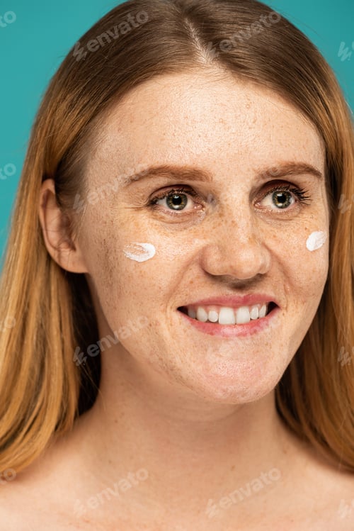 Preview: closed up of happy woman with freckles and cream on face isolated on turquoise