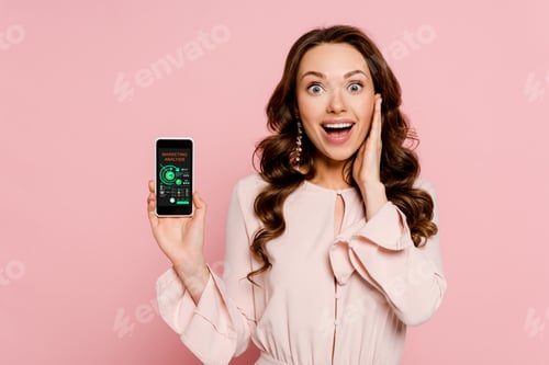Preview: excited girl holding smartphone with charts and graphs on screen and looking at camera isolated on
