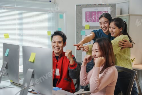 Preview: Excited asian coworkers celebrating success looking at computer screen in office