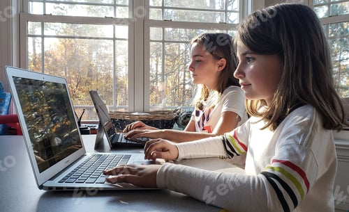 Preview: Natural light in playroom where Gen z sisters do school work on mobile devices using hands.