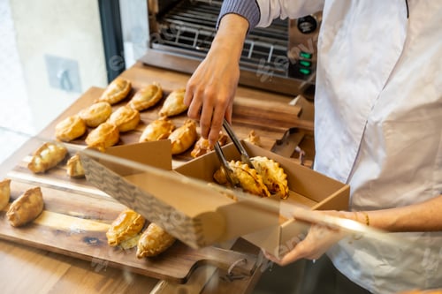 Preview: Baker packaging freshly baked empanadas into a take out box