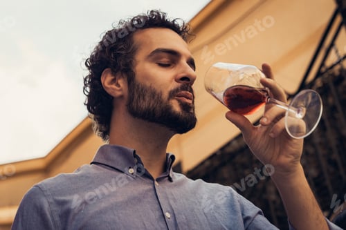 Preview: Young man smelling red wine in glass during outdoor wine tasting