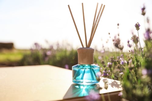 Preview: Reed air freshener on wooden table in blooming lavender field. Space for text