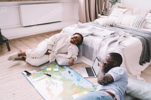 Preview: Cheerful black couple relaxing on floor with laptop at home
