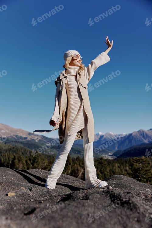 Preview: young woman in autumn clothes stands on a rock blue sky lifestyle