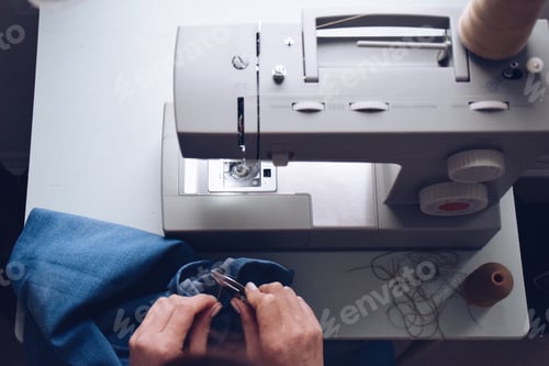Preview: Seamstress is cutting a thread on the jeans she is hemming on sewing machine