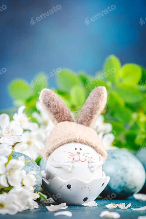 Preview: Easter rabbit figurine, blue painted eggs, white cherry flowers with leaves on blue background