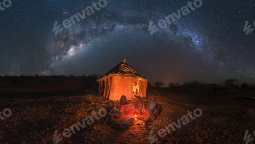 Preview: Panoramic view of four African women sitting around fire with camp in their back under a sky