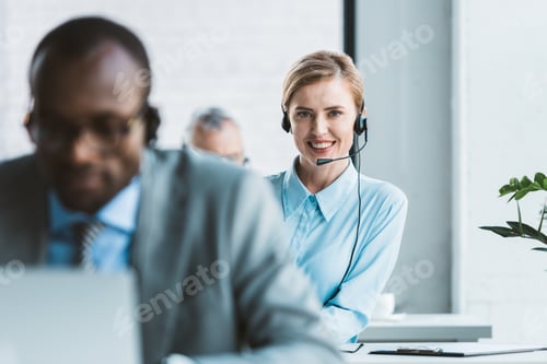 Preview: selective focus of attractive businesswoman in headset smiling at camera