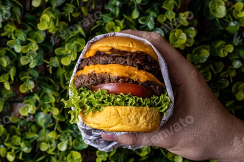 Preview: Appetizing hamburger wrapped in foil paper, held by a male hand
