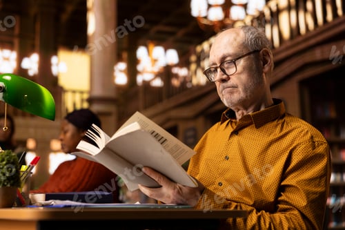 Preview: Elderly retired old man paying attention to reading hobby at the public library,