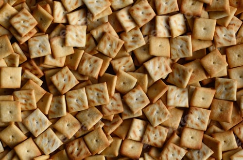 Preview: A lot of small cookies are square shaped. A pattern of a yellow salt cracker