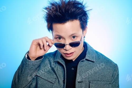 Preview: Stylish young asian man with sunglasses shows confidence in bright blue background