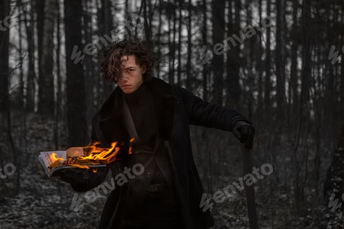Preview: A Caucasian guy, a teenager, with long curly hair stands in the forest with a burning book