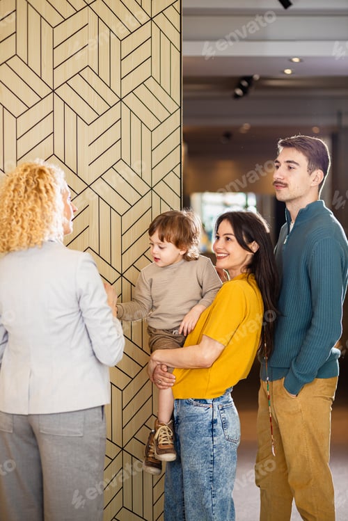 Preview: Saleswoman showing a young couple with a child the panels for decorating the interior of the home.