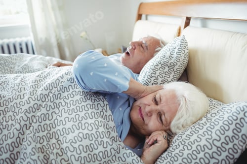 Preview: Man snoring and woman covering her ears while sleeping on bed