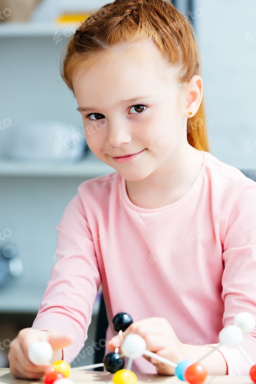 Preview: beautiful redhead schoolgirl holding molecular model and smiling at camera