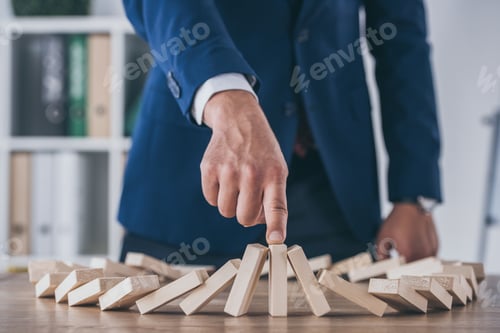 Preview: cropped view of risk manager stopping domino effect of falling wooden blocks