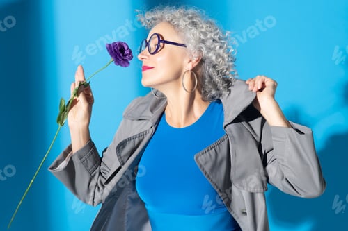 Preview: Curly woman wearing blue dress smelling nice flower