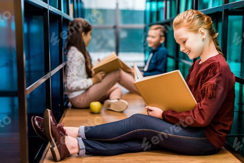 Preview: adorable schoolchildren sitting on floor and reading books in library