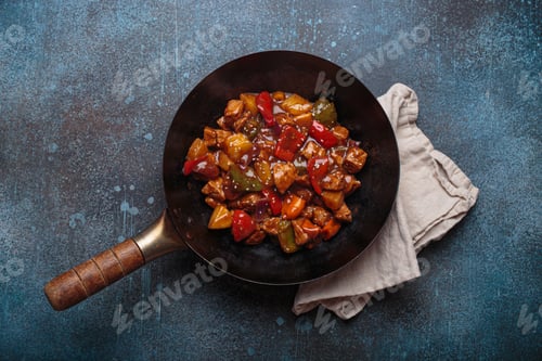 Preview: Sweet and sour pork in wok pan with peppers and pineapple top view, traditional Chinese dish
