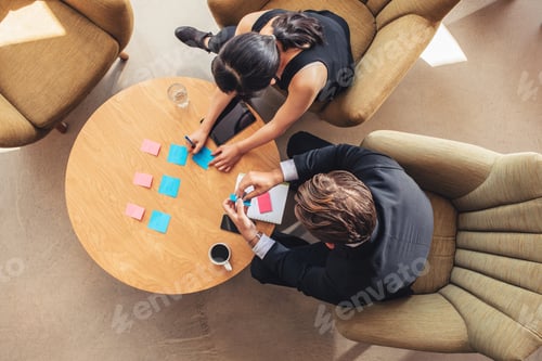 Preview: Businesspeople discussing over adhesive notes in office lobby
