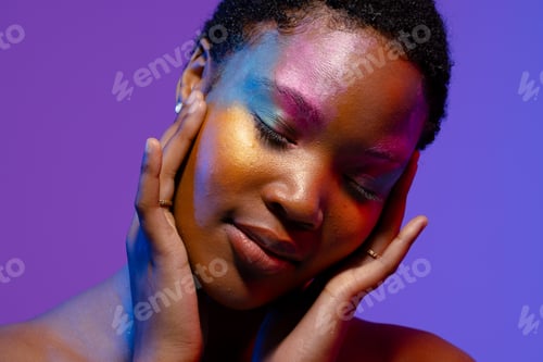 Preview: African american woman with short hair and colourful make up touching face with eyes closed