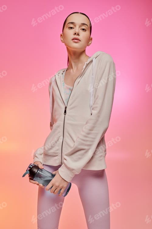 Preview: Stylish woman in workout attire stands confidently against a vibrant pink and orange backdrop