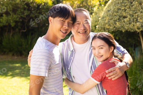 Preview: Smiling father and teenage son and daughter hugging outdoors, enjoying time together in garden