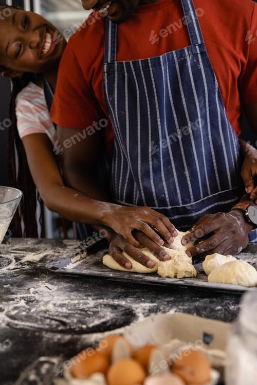 Preview: Happy african american couple in aprons preparing bread dough in kitchen