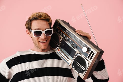 Preview: Ginger young man wearing sunglasses posing with retro tape recorder