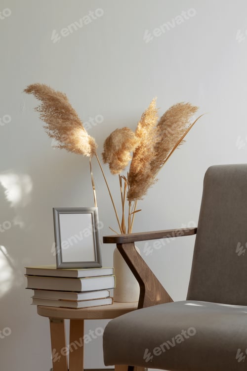 Visualização: Mesa de madeira com pilha de livros e vaso com capim-dos-pampas, mockup de moldura cinza, cadeira cinza