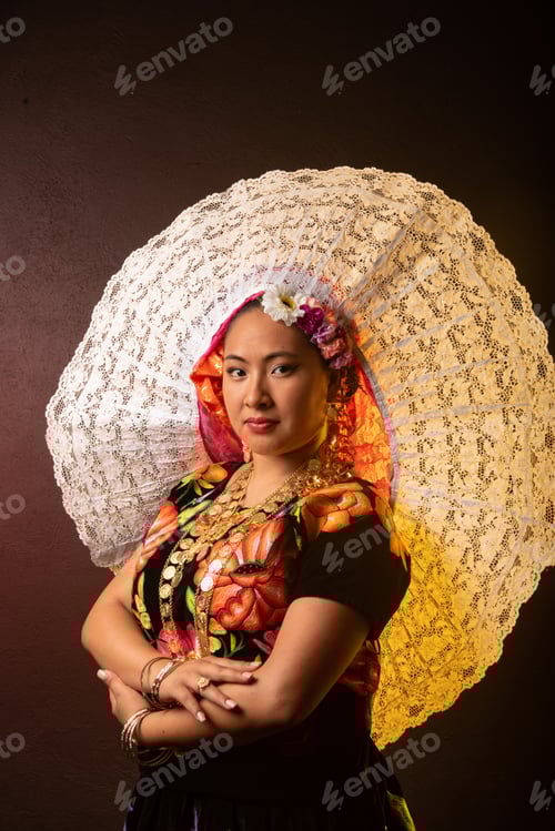 A woman wearing a flowery hat and a colorful dress poses for a photo