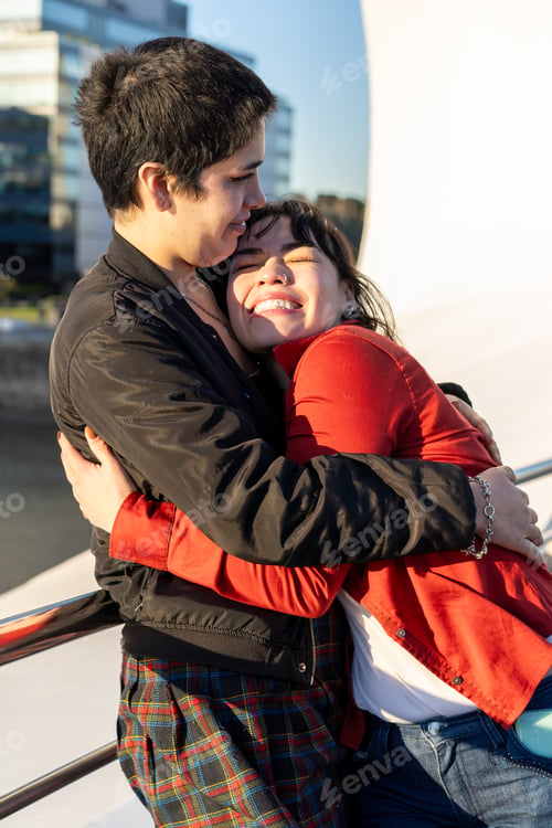 Preview: Young LGBT couple of women embracing each other on a bridge, capturing a moment of affection