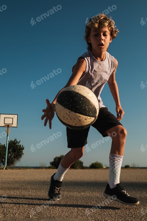 Preview: Focused boy in sportswear dribbling basketball