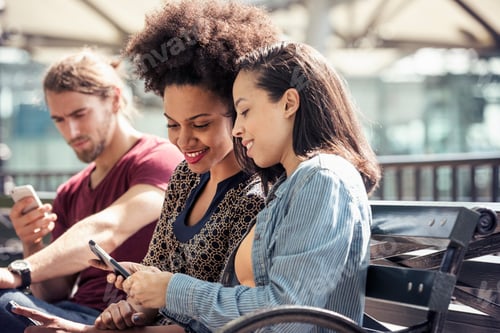 Preview: Three people seated side by side on a park bench checking their smart phones