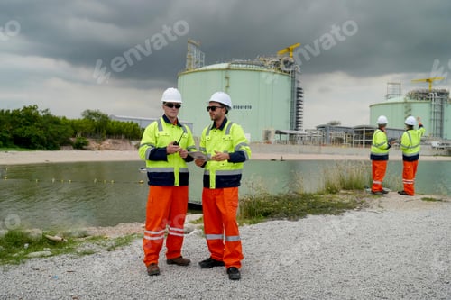 Preview: Workers discuss project by industrial facility near water under stormy sky